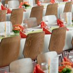 Beautifully arranged tables with wooden chairs for a formal event, adorned with orange flowers.