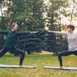 Pretty women is trendy sports clothing are training outdoors doing yoga enjoying movement, fresh air and warm autumn weather. Sports, leisure and youth concept.