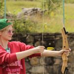 A young adult practicing archery outdoors in a casual setting, focusing on technique.